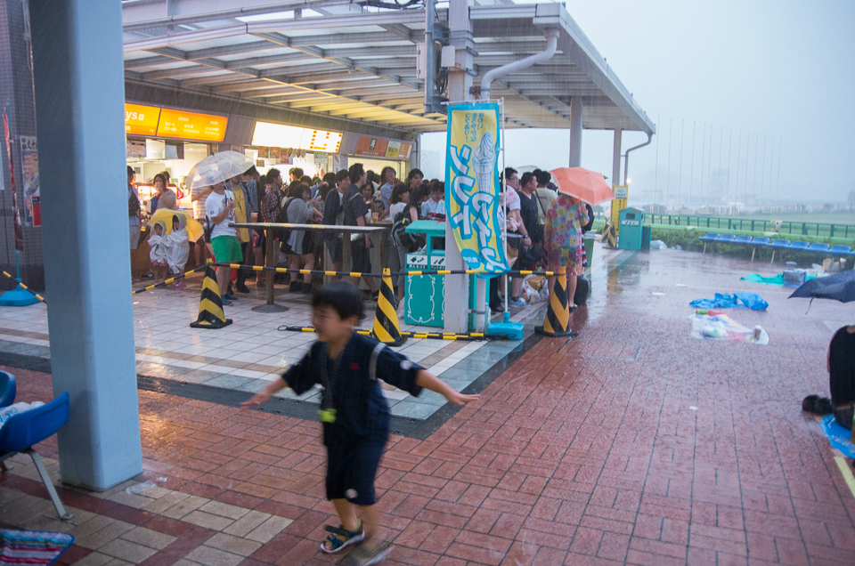 激しい風雨に、馬券売場や売店の軒下に逃げ込む人々。子供は元気！